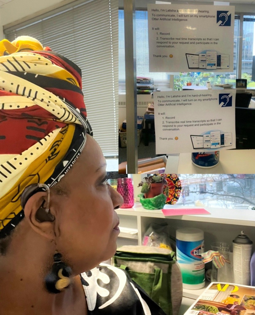 Black woman wearing a head wrap and hearing aids looks away from the camera to signage that guides folks how to effectively communicate with her.